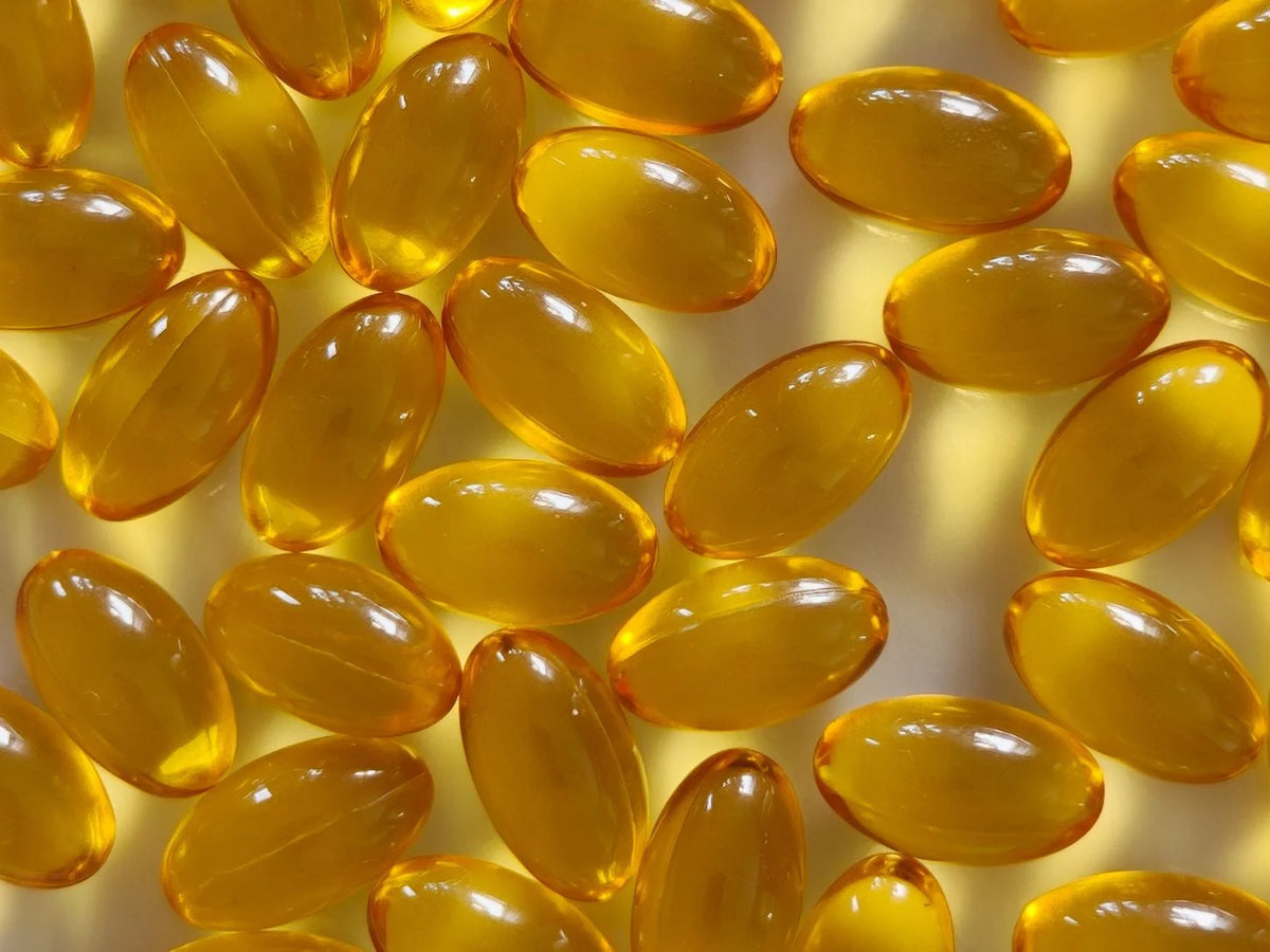 Viele goldgelbe Vitamin-D3+K2-Weichkapseln im Gegenlicht, Nahaufnahme