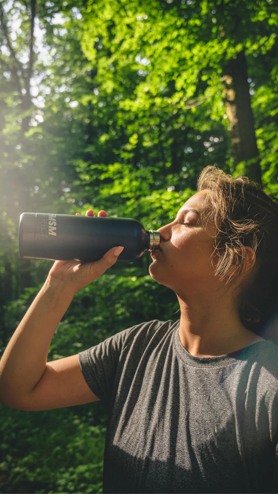 Frau trinkt im Wald aus einer Trinkflasche