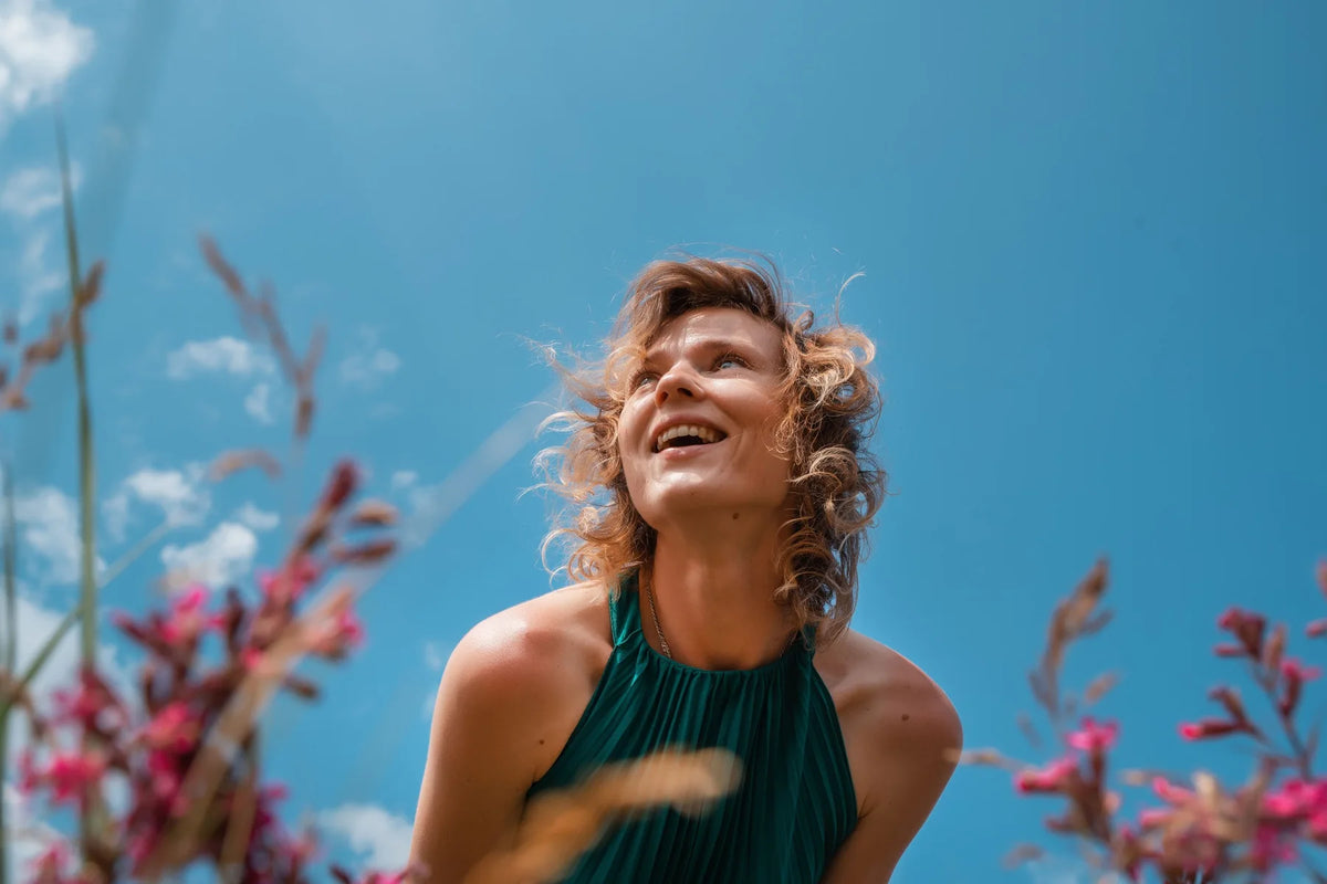 Lachende Frau schaut im Sommer in den blauen Himmel