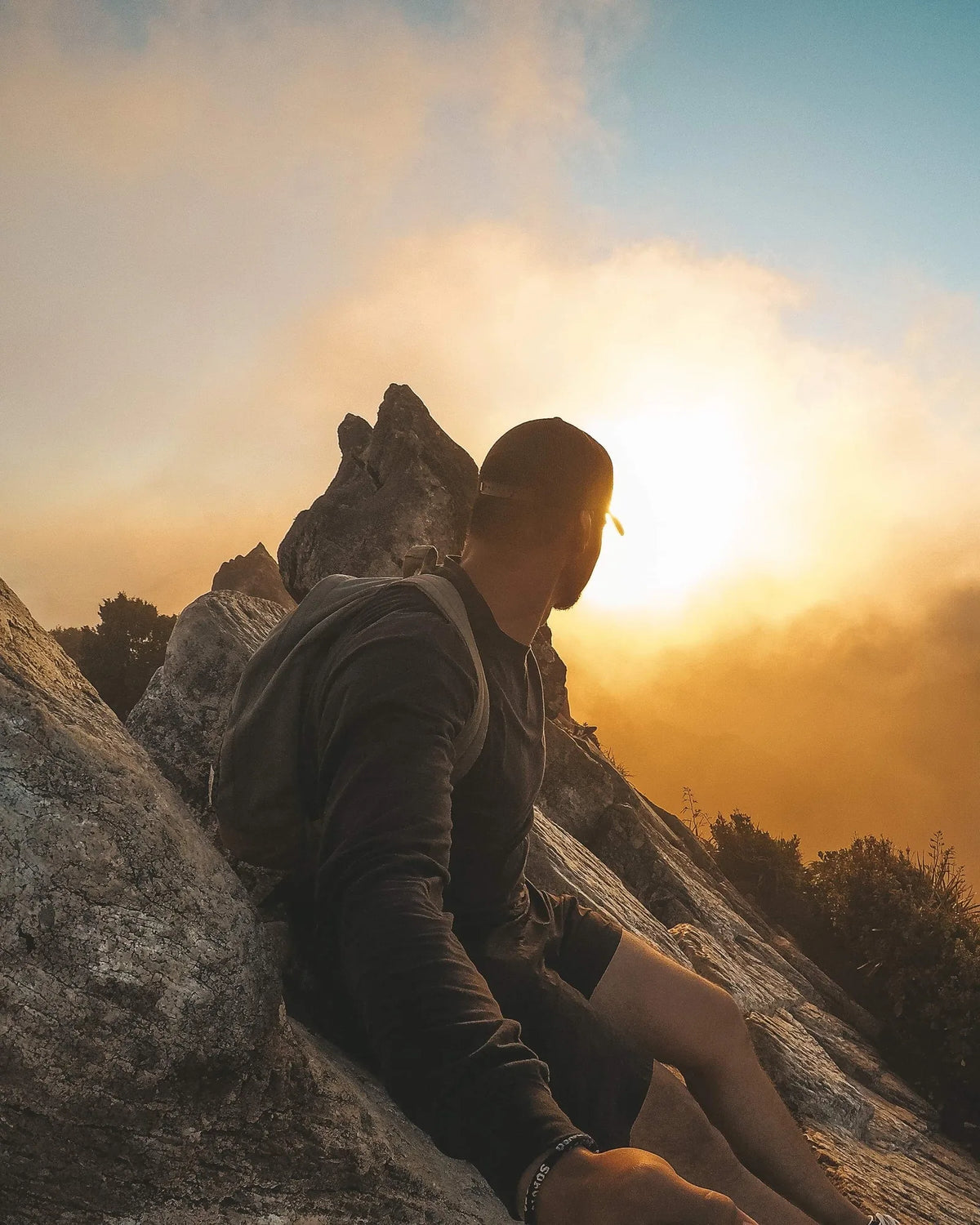 Mann sitzt auf einem Felsen und schaut in den Sonnenaufgang über den Wolken