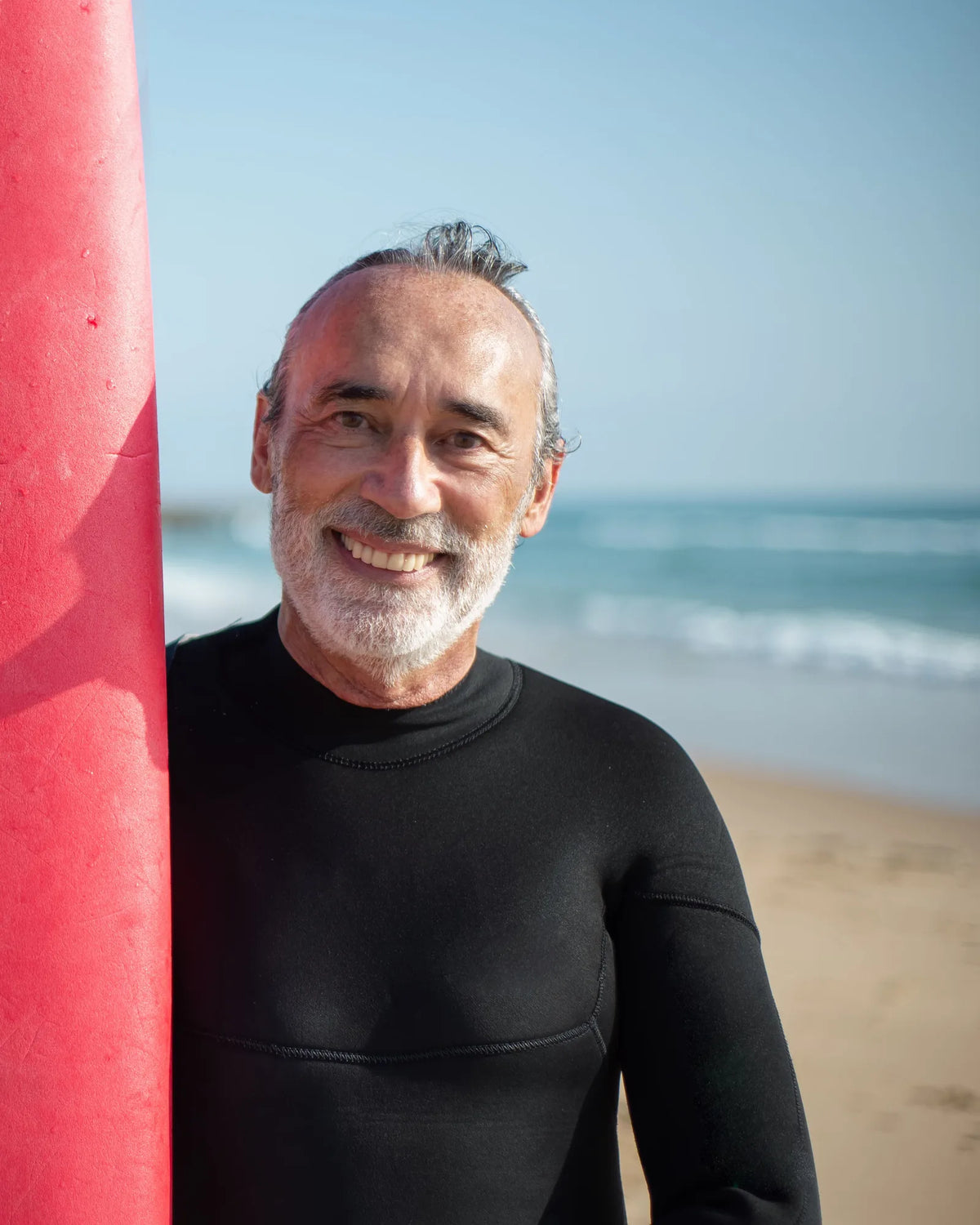 Lächelnder älterer Mann im Neoprenanzug mit Surfbrett am Meer