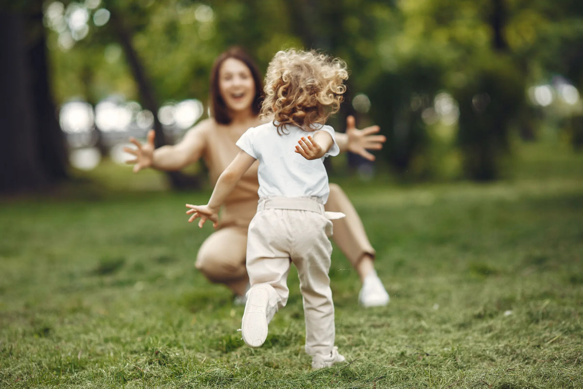 Kleines Kind läuft lachend in die ausgebreiteten Arme seiner Mutter auf einer Wiese