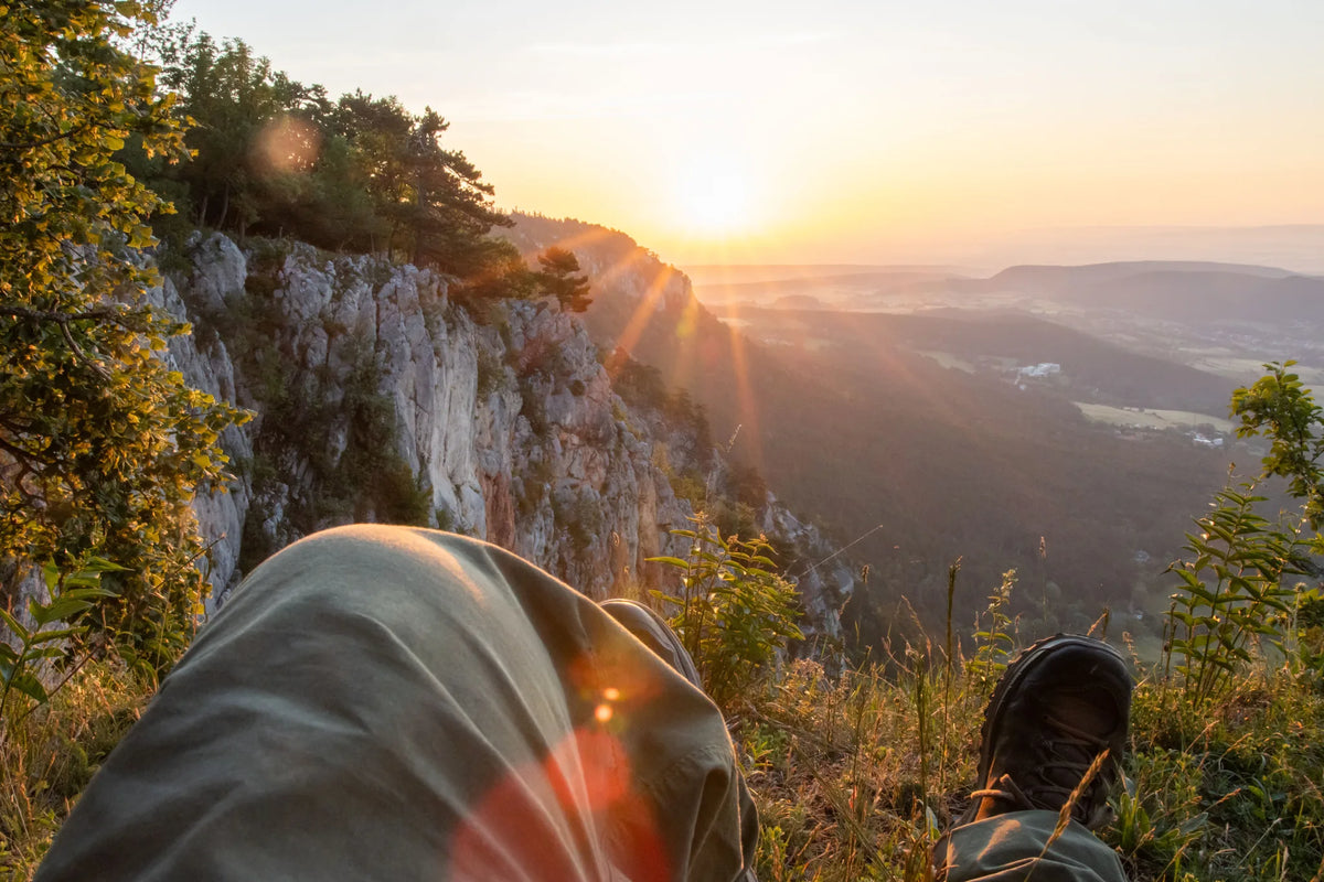 Rast auf einem Felsvorsprung mit Blick über Berge im Sonnenuntergang