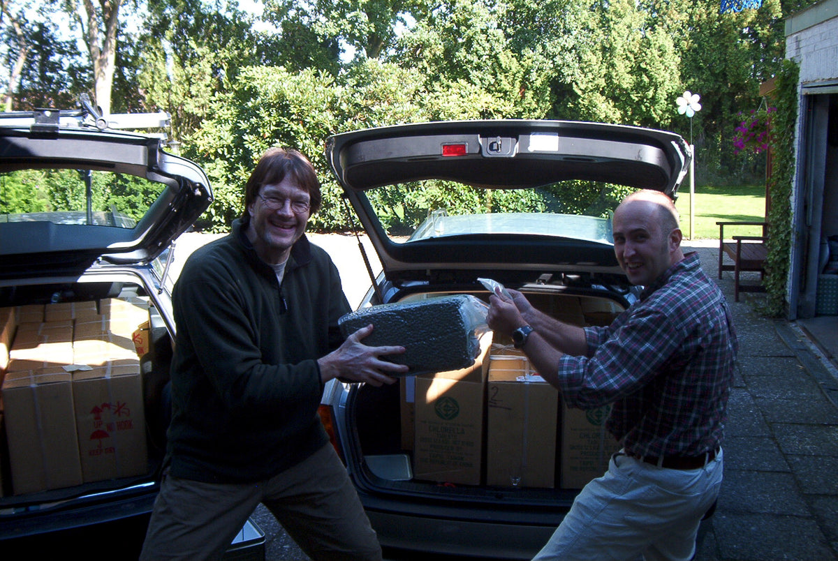 Holger Cremer und Dr. Frank Liebke mit Chlorella-Kartons an zwei geöffneten Autos.